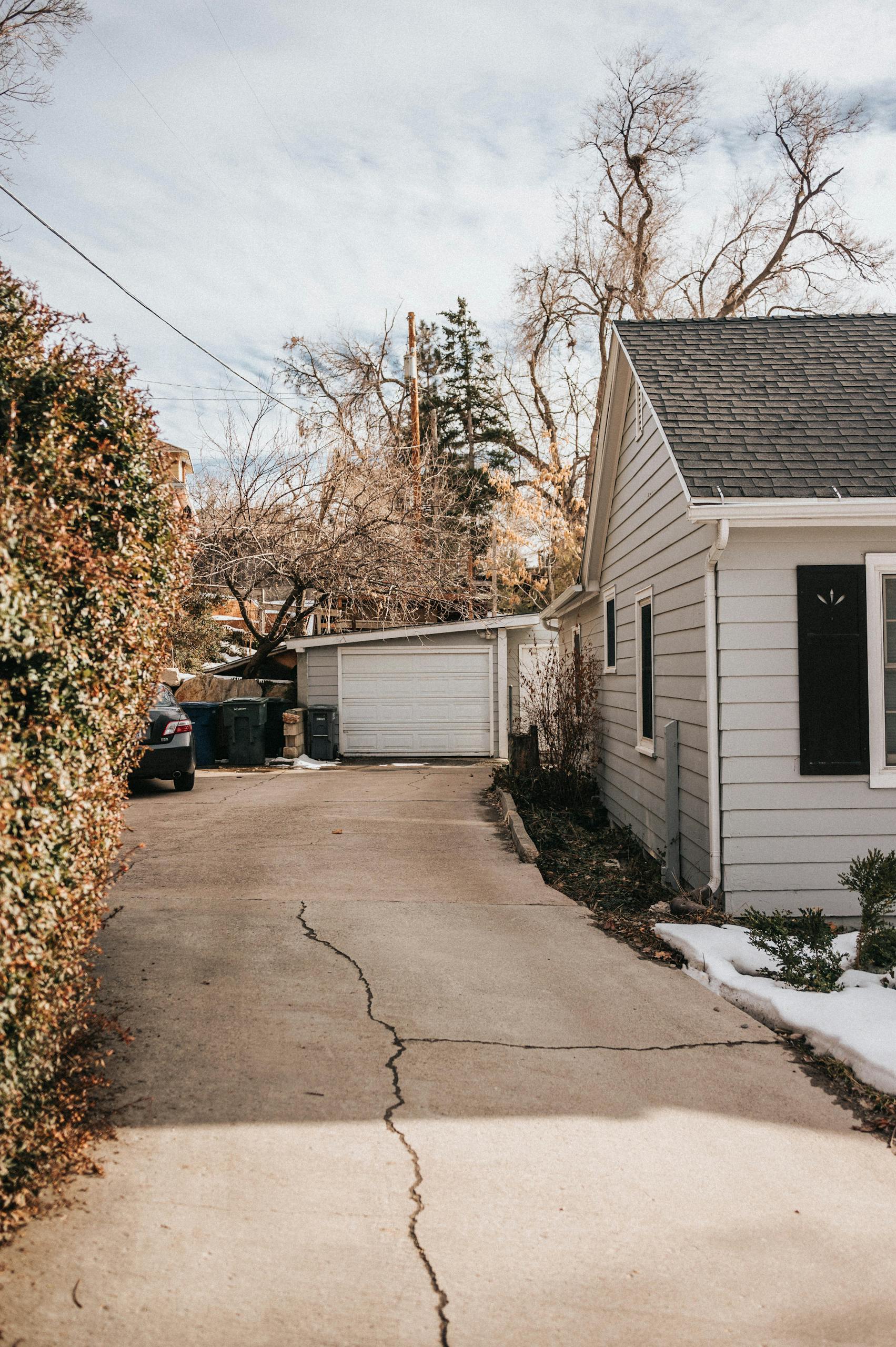a peaceful suburban driveway with cracked pavement leading to a house surrounded by bare trees 15913566 scaled 1
